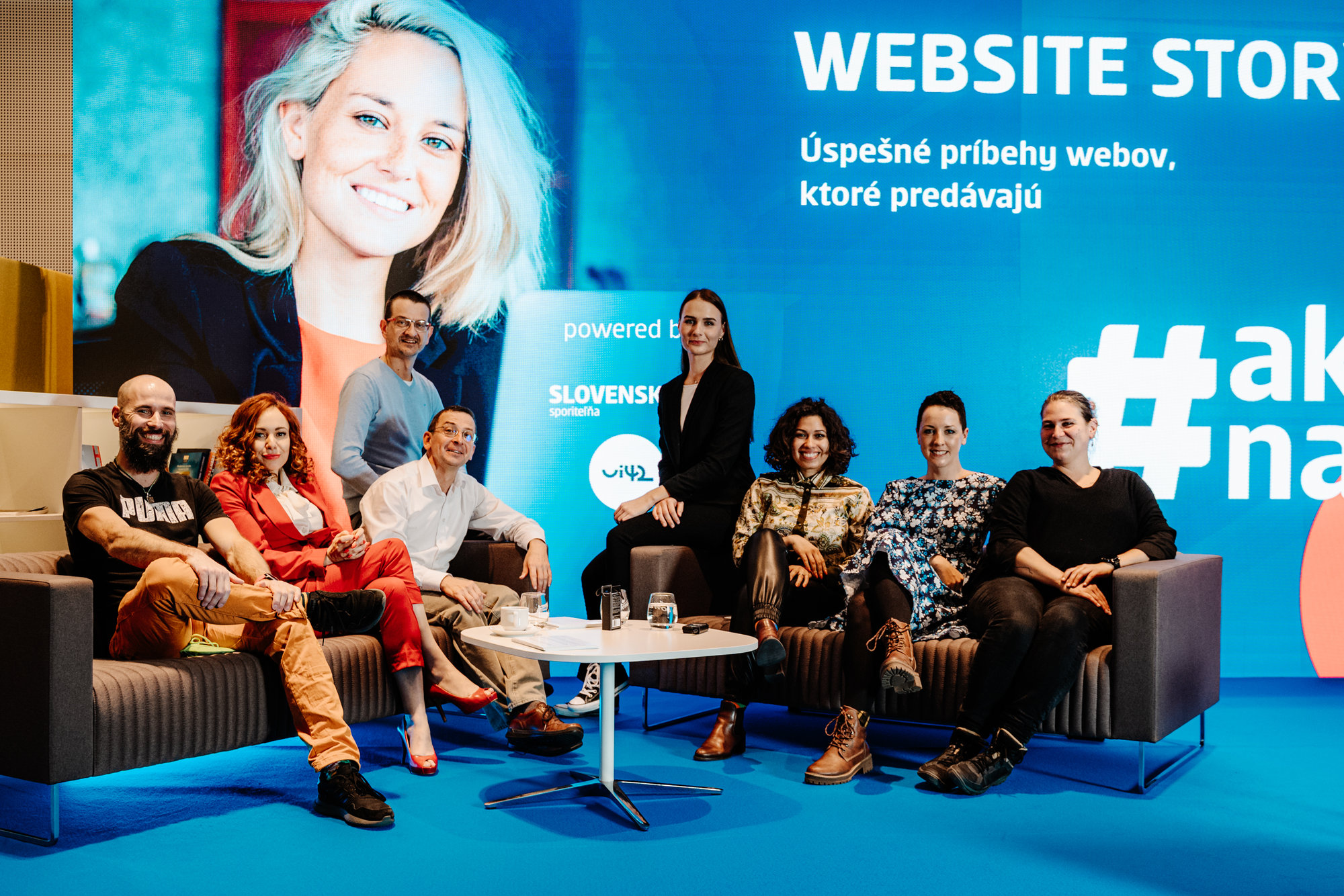 Skupina ľudí sediaca na pódiu pred veľkou obrazovkou s nápisom 'Website stories: Úspešné príbehy webov, ktoré predávajú'.