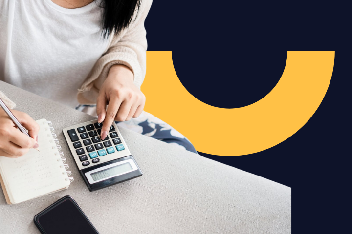 Osoba píše do zápisníka a používa kalkulačku, vedľa je položený mobil