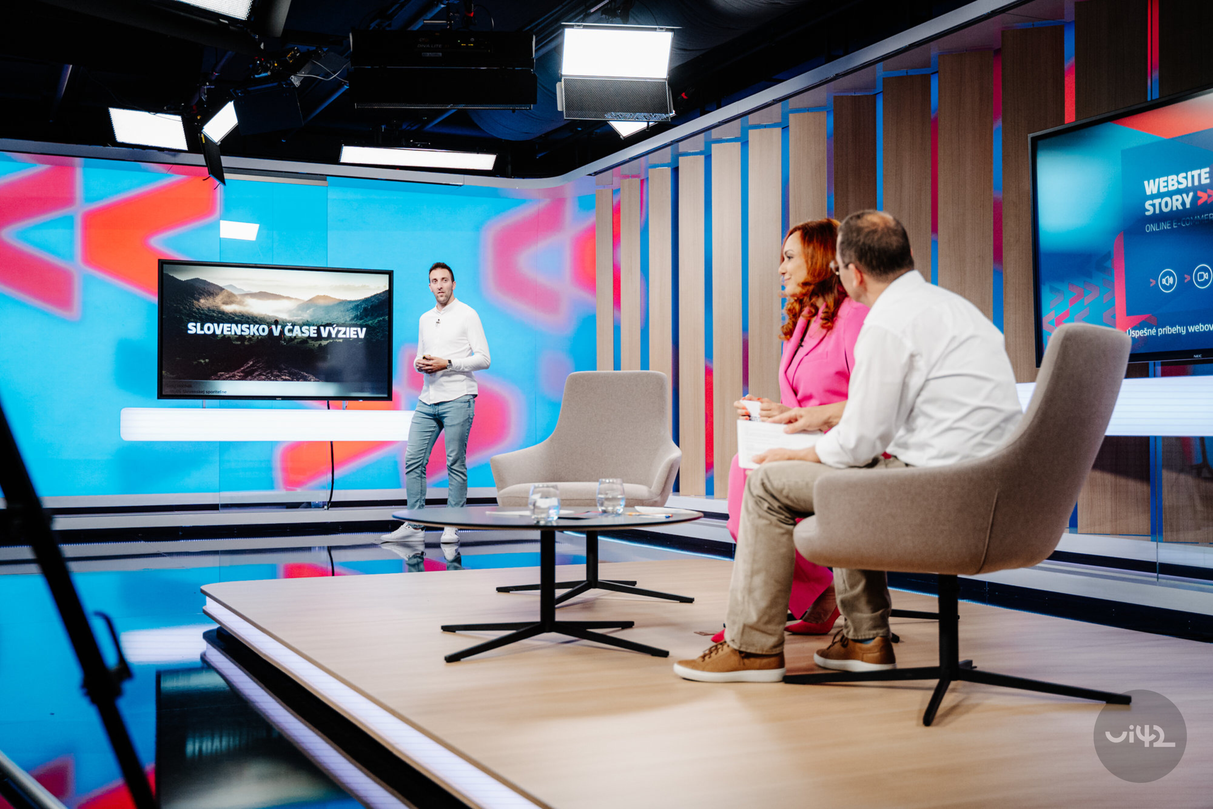 Televízne štúdio s tromi ľuďmi diskutujúcimi pred obrazovkou s nápisom 'Slovensko v čase výziev'.