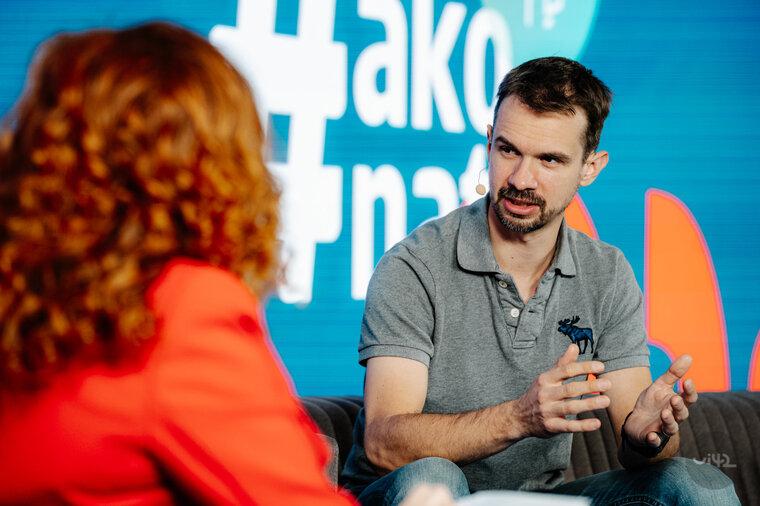 Dvojica diskutuje počas online konferencie, muž v šedom tričku gestikuluje, žena s ryšavými vlasmi v červenom saku počúva.