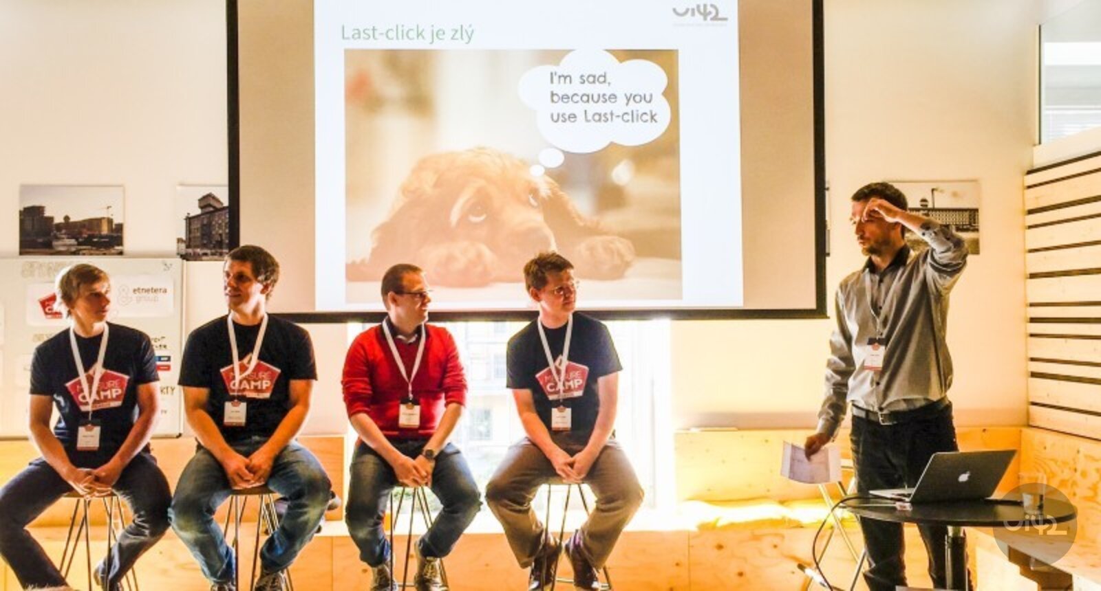 Prednáška na podujatí MeasureCamp na Slovensku, kde štyria účastníci sedia na stoličkách a jeden prednášajúci stojí vedľa projektora.